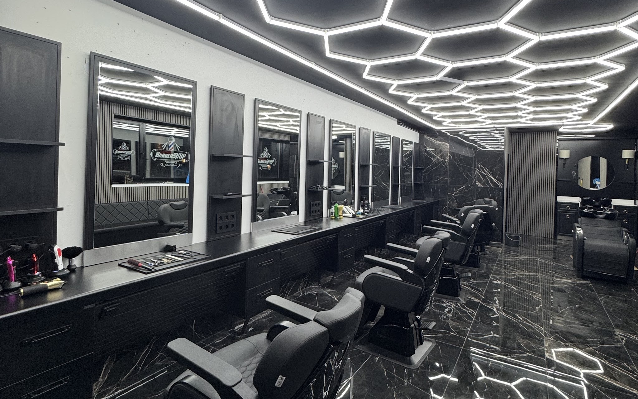 De zaak van Cousin barbershop: zeshoekig lichtplafond, lange spiegelwand en zwarte barberstoelen op een marmeren vloer