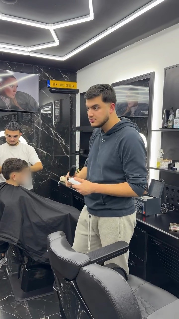 Barber bij zijn werkplek met tondeuse in de hand, op de achtergrond een collega aan het knippen